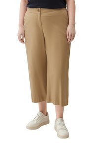 Culotte pants in light brown, made of smooth fabric, featuring a button closure and wide, cropped legs. Worn with white sneakers.