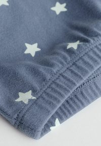 Gros plan sur un tissu bleu avec des motifs d'étoiles blanches et des coutures de poignet en élastique côtelé sur un vêtement.