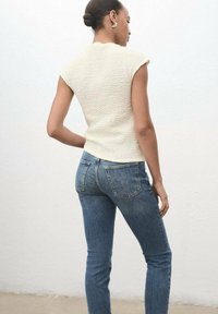 Top corto a maniche corte di colore crema con finitura testurizzata abbinato a jeans blu aderenti. Entrambi i capi evidenziano una silhouette aderente e dettagli minimi.