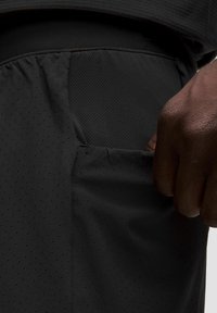 Shorts sportivi neri con tasca in rete testurizzata e traspirante. Il tessuto è leggero con una finitura liscia, mostrando sottili perforazioni.