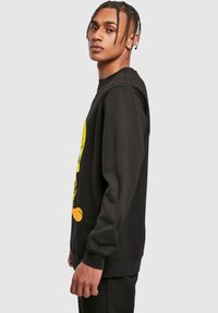 Felpa nera con una grande grafica di un personaggio dei cartoni animati giallo sul fronte, polsini a costine e un design dalla vestibilità rilassata.