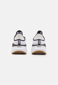 Des chaussures de sport blanches et noires avec une tige en mesh, une languette arrière et une semelle grise texturée avec des accents en caoutchouc gomme. Marque "SOFTRIDE" visible.