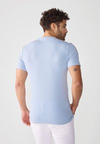Tricou bleu deschis cu mânecă scurtă, fabricat dintr-un material moale, având guler rotund și o siluetă ajustată. Fără modele sau grafică vizibile.