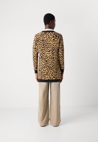 Pulover z dolgimi rokavi v leopardjem vzorcu z bež osnovo in črnimi pikami, ki ima črno rebrasto spodnji del in manšete, v kombinaciji s svetlobež širokimi hlačami.