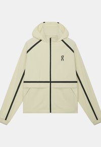 Veste à capuche beige clair avec des bandes noires le long des manches, de la poitrine et de la fermeture éclair, avec un petit logo noir sur le côté gauche de la poitrine.