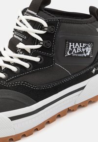 Mustad mustad sneakerid valgete nööridega, nahast ja tekstiilist ülemine osa, kummist tald, millel on kummitread ja must logoplaat küljes.