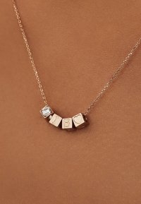 Collier en or rose avec blocs de lettres gravées et cœurs, doté d'un détail en zircon cubique, suspendu à une chaîne délicate.