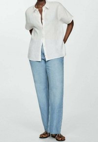 White linen short-sleeve shirt with a button-down front, paired with high-waisted light blue wide-leg jeans and brown sandals.