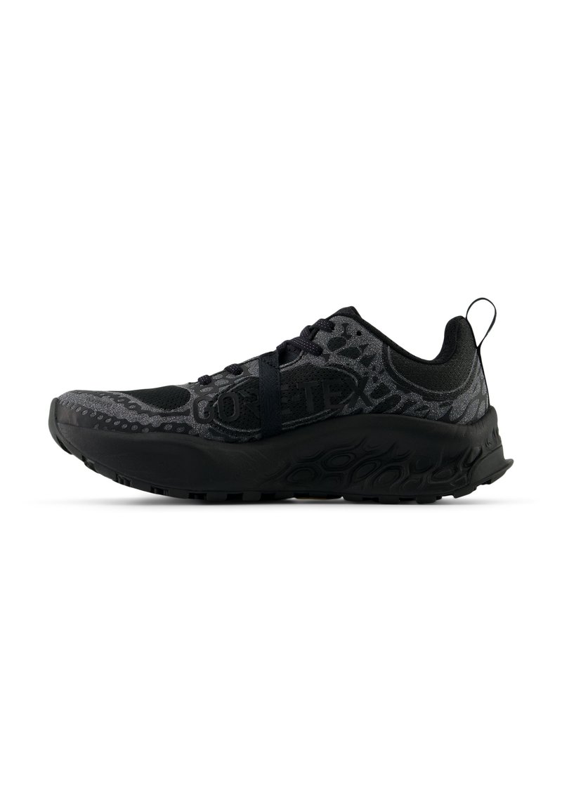 Chaussure de sport noire avec un dessus texturé, un orteil renforcé et une semelle amortissante. Présente une étiquette Gore-Tex et un design de lacets minimaliste.