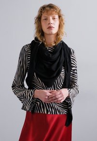 Čierny šál prehodený cez pruhovaný čierno-biely top s dlhým rukávom, v kombinácii s červenou sukňou. Top má rozšírené rukávy a vysoký golier.