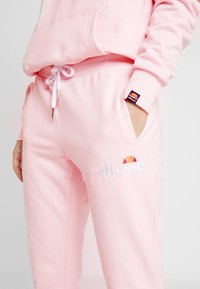 Ljust rosa sweatpants i mjukt tyg, med resårmidja med snörning, sidofickor och en broderad logga.