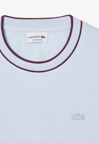 Polo shirt azzurro chiaro con colletto a coste color borgogna. Presenta un tessuto texture e un piccolo logo ricamato sul lato sinistro. Vestibilità regolare.