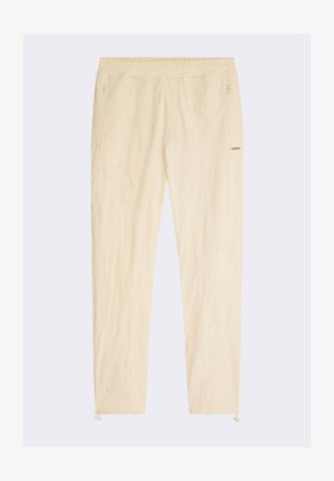Pantalones tapered de color beige claro con una cintura elástica, que presentan patrones de costura sutiles y un bolsillo con cremallera en el lado derecho.