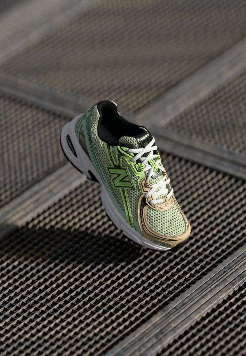 lichtgroene en beige mesh sportshoe met witte veters en een dikke witte zool, rustend op metalen rooster.