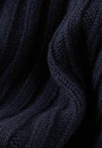 Zacht, donker marineblauw gebreid stof met zichtbare geribbelde textuur en zachte plooien die diepte en schaduw creëren.