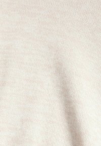 Tissu tricoté beige clair avec une texture fine, présentant un motif uniforme et une apparence douce et lisse. Idéal pour les vêtements.