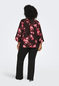 Black floral kimono-style top with pink and red flower patterns, paired with black pants. Textured fabric and wide sleeves.
