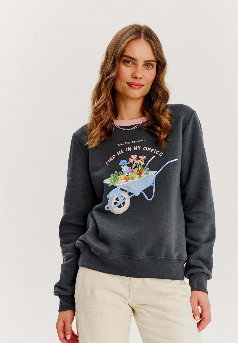 Tmavohnedá mikina s grafickým motívom svetlomodrej vozíka plnej kvetov. Rúbkované manžety a lem, ružový akcent na golieri a text nad dizajnom.