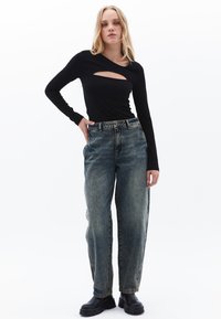 Schwarzes Langarmoberteil mit Ausschnitt, kombiniert mit lockeren, ausgewaschenen blauen Jeans. Das Model trägt schwarze Plateaustiefel. Einfache, lässige Stil.