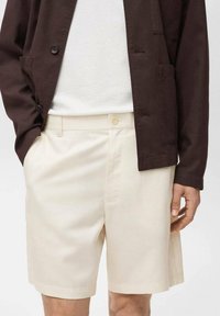 Beige shorts med lige pasform, lavet af letvægtsstof. Har en enkelt knaplukning og sidelommer. Bæres med en mørk jakke.