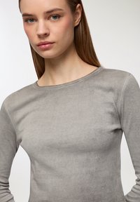 Szary długi rękaw z gładką, miękką fakturą i okrągłym dekoltem, o dopasowanym kroju i minimalnych szwach dla uzyskania smukłego wyglądu.