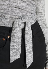 Top grigio mélange a maglia con dettaglio in vita annodato, abbinato a jeans di denim neri con dettagli in ottone sui bottoni.
