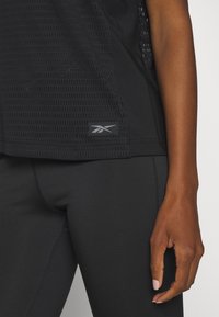 Svart sporttopp med en texturerad design och mönstrade meshavsnitt, tillsammans med svarta leggings. Inkluderar en märkeslogotyp.