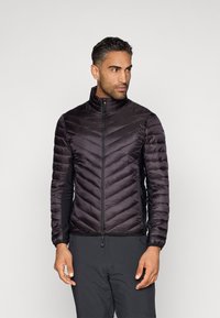 Melnā puffer jaka ar chevronam līdzīgu quilted dizainu un stāvošu apkakli. Iezīmēta ar rāvējslēdzēja aizdari un kontrastējošiem melniem sānu paneļiem.