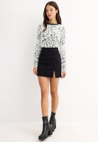 Suéter de manga larga blanco y negro con un patrón, combinado con una mini falda negra con una abertura lateral. La modelo lleva botines negros de tacón cuadrado.