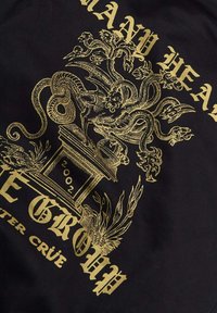 Tessuto nero con elaborati ornamenti dorati che raffigurano un serpente con più teste sopra un piedistallo ornato, con i numeri "2002" e accenti floreali.