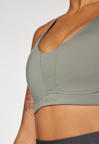 Sutiã esportivo verde com decote em V, painéis texturizados e perfurações para respirabilidade. Logótipo "BORG" exposto na faixa.