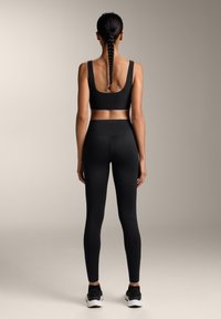 Črn sklop aktivne obleke, ki vključuje oprijet športni top z širokimi naraminicami in visokim pasom, prikazan na nevtralni podlagi.