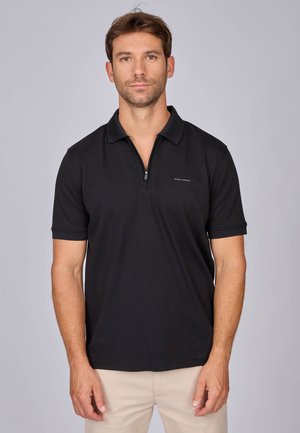Polo noir avec une fermeture éclair mi-hauteur, un col texturé et des manches courtes. Possède un petit logo sur la poitrine gauche. Tissu en mélange de coton lisse.
