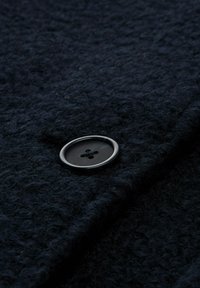 Marineblauer strukturierten Stoff mit einem großen schwarzen Knopf mit vier Löchern, teilweise gefaltet, um die Details hervorzuheben.