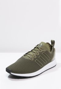 Olivgrön sportskor med en texturerad mesh-övre, tre-randig design på sidorna och vit gummisula. Ögla på hälen för enkel påklädning.