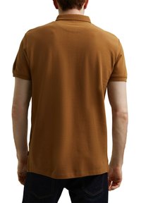 Polo marron avec un col structuré, des manches courtes et un ourlet droit. Fabriqué en tissu de coton avec une texture lisse.