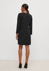 Schwarzes langärmeliges Kleid mit geradem Schnitt, ausgestattet mit einem Reißverschluss im Rücken und einem knielangen Saum. Glatte Textur und minimales Design.