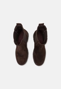 Stivaletti alla caviglia in pelle scamosciata marrone con pannelli laterali elastici, punta rotonda e superficie texturizzata. Design minimalista con cuciture tono su tono e suola piatta in gomma.