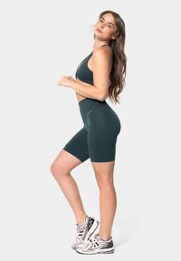 Donkerblauwe sportoutfit bestaande uit een aansluitende sportbeha en high-waisted fietsbroek. Het materiaal is rekbaar met een gestructureerd patroon. Schoenen zijn zilver en zwart.
