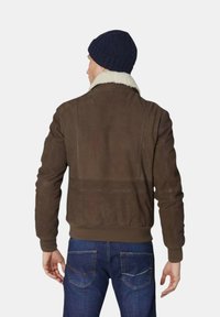 Bruine leren bomberjack met een schapenleren kraag, geribbelde manchetten en tailleband; gecombineerd met blauwe spijkerbroek.