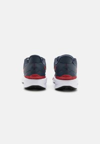 Des chaussures de sport bleu et rouge présentent une tige en maille texturée, un col rembourré, une semelle intermédiaire blanche et une semelle extérieure en caoutchouc noir avec un motif distinctif.