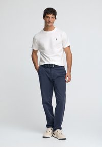 Biała bawełniana koszulka, granatowe spodnie, czarny pasek, beżowe trampki. Prosty design; dopasowana koszulka z małym logo; spodnie o luźnym kroju.