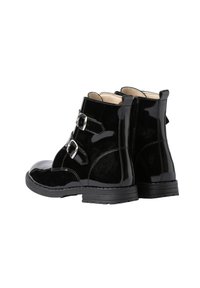 Botas de tobillo de charol negro con dos hebillas plateadas en el lado exterior y un tacón bajo apilado sobre un fondo blanco.