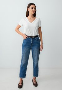 T-shirt bianco a scollo a V abbinato a jeans in denim blu a vita alta. Vestibilità classica con una leggera trama; include una cintura marrone e scarpe scure.