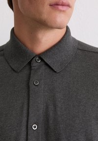 Szara koszulka polo o miękkiej fakturze, z klasycznym kołnierzykiem, plisą na trzy guziki oraz kontrastującymi czarnymi guzikami.