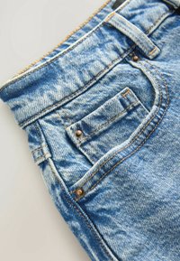 Hellblaue Jeans aus Denim mit sichtbaren Nähten, einer vorderen Tasche und Metallnieten. Der Stoff weist eine leicht abgenutzte Textur mit verblasstem Aussehen auf.