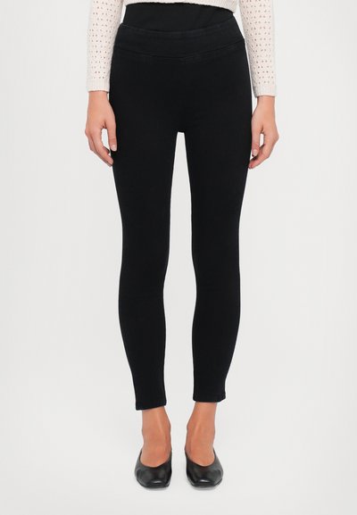 Schwarze Leggings aus dehnbarem Material, mit hohem Bund und enganliegender Passform, die bis zu den Knöcheln reicht. Glatte Textur ohne Muster.
