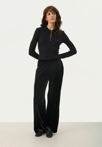 Top negru cu dungi, cu mânecă lungă și detalii cu nasturi, asociat cu pantaloni negri din catifea cu picior larg și pantofi negri slip-on cu ținte.