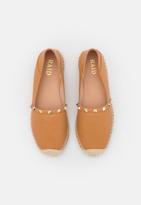 Scarpe slip-on in pelle tan con suola in stile espadrillas intrecciata. Presentano una fila di borchie dorate a forma di piramide lungo la parte superiore. Logo del brand visibile all'interno.
