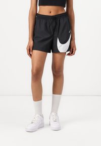 Melni sporta šorti ar elastīgu jostasvietu, ar lielu balto Nike swoosh un sānu šuvju kabatām. Apvienoti ar baltām kedām un zeķēm.